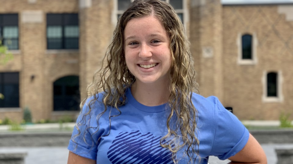 A student standing in front of Arkport CSD with her hand on her hip and a blue tee shirt that says "Dissent is patriotic"