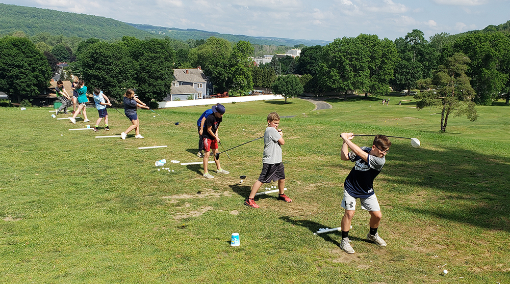 Six students standing in a row practicing their golf swing