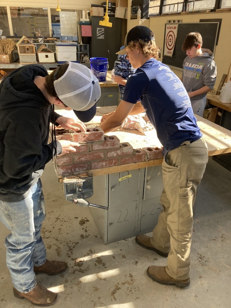 Two students building a brick wall in masonry class.