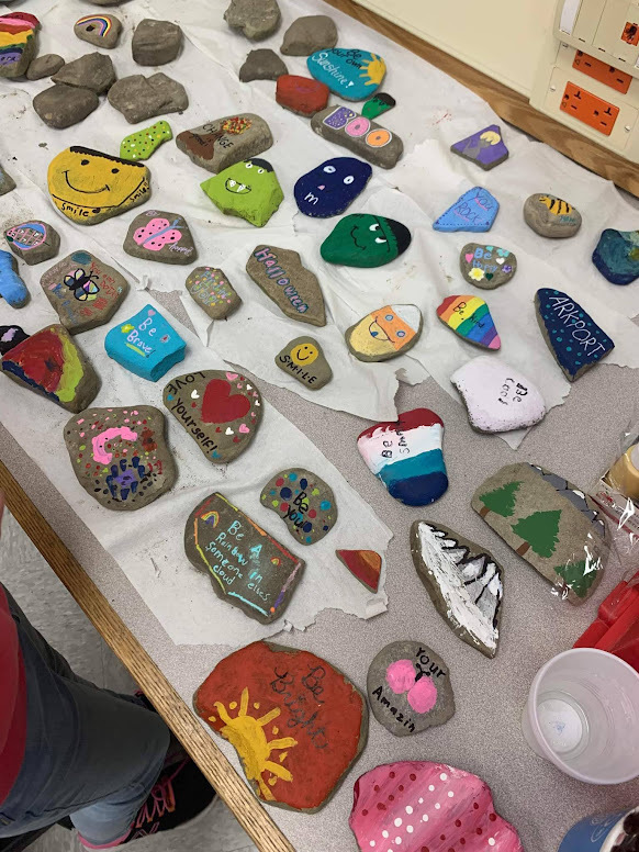 Rocks spread on a table, after students painted them with inspirational messages.