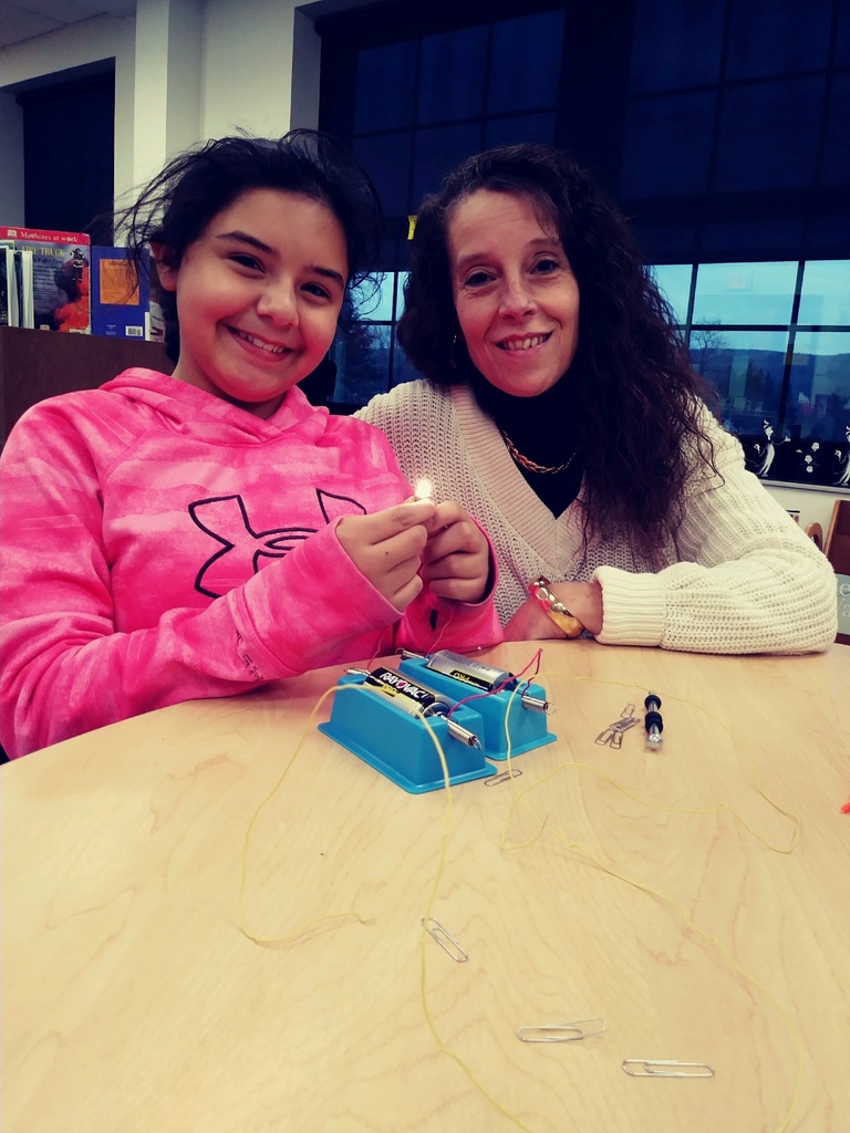 Student and teacher smiling at the camera as they work together on electromagnetism force. 